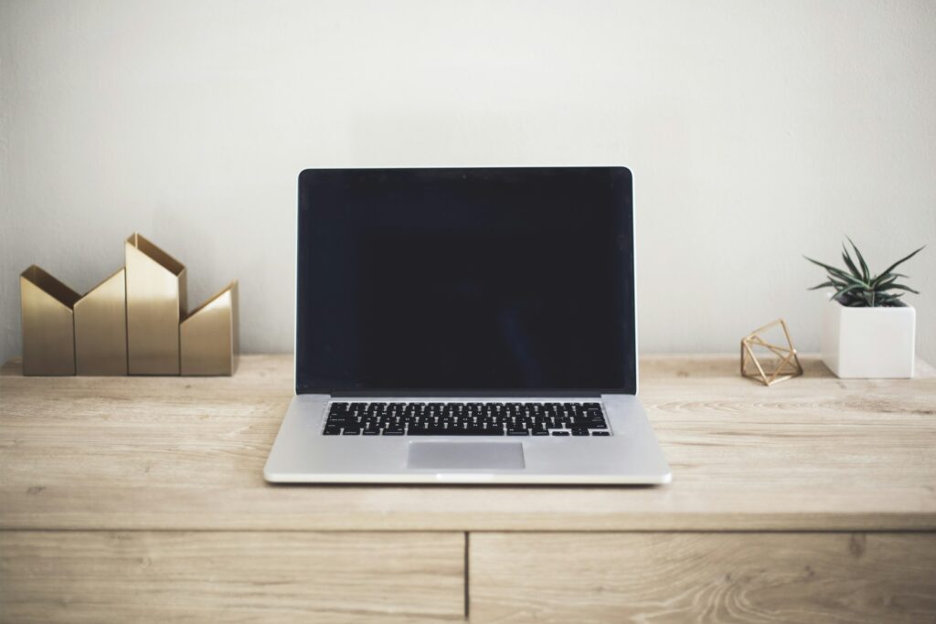 A tidy desk with a laptop, a plant and small brass ornaments